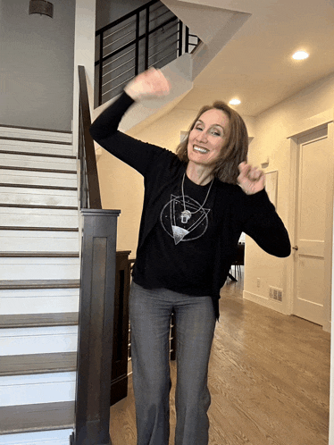 a woman wearing a black sweater and grey pants is standing in front of stairs