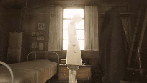 a woman in a white dress is standing in front of a window in a bedroom