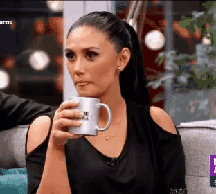 a woman is sitting on a couch holding a coffee mug and making a face .