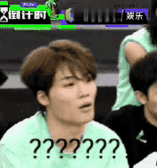 a man in a green shirt is sitting in front of a group of people and making a surprised face .