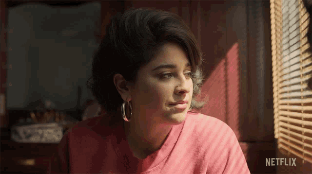 a woman in a red shirt is sitting in front of a window with blinds and the word netflix on the bottom