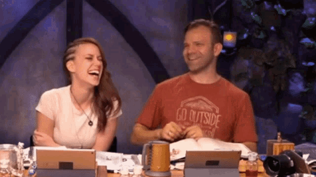a man and a woman are laughing together while sitting at a table .