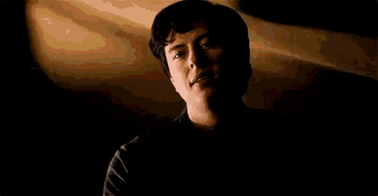 a man is sitting in a dark room with his head down and his eyes closed .