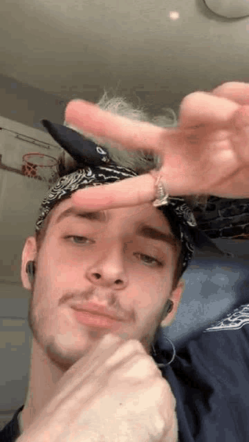 a young man wearing a bandana and earrings is making a peace sign with his hand .