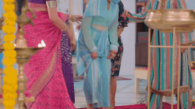 a woman in a blue saree is standing in a room with other women in colorful dresses .
