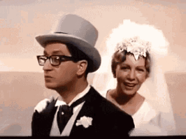 a man in a tuxedo and top hat is standing next to a bride in a wedding dress .
