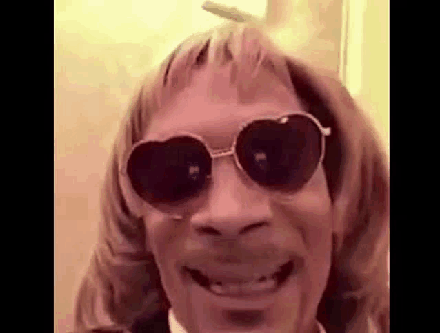 snoop dogg is wearing sunglasses and a wig and smiling .