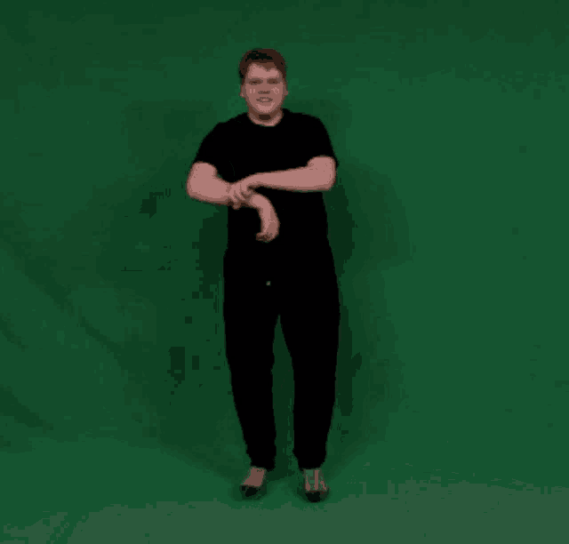 a man in a black shirt and black pants stands in front of a green screen