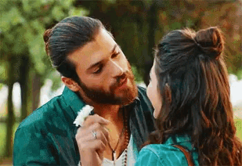 a man with a beard is holding a flower and kissing a woman on the cheek .