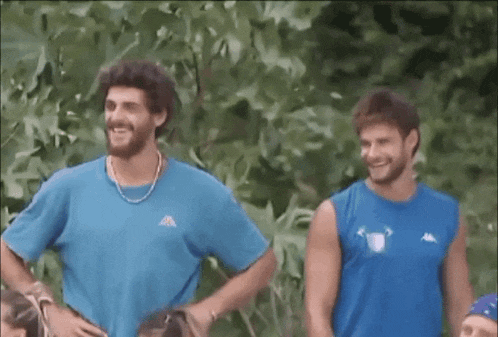 two men are standing next to each other and smiling . one of the men is wearing a kappa shirt .