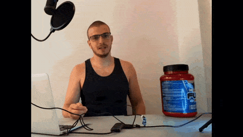 a man is sitting at a desk with a microphone and a container of protein