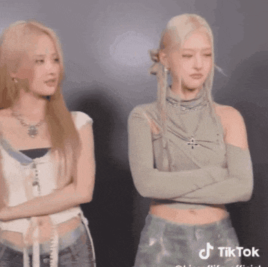 two women are standing next to each other with their arms crossed and looking at each other .
