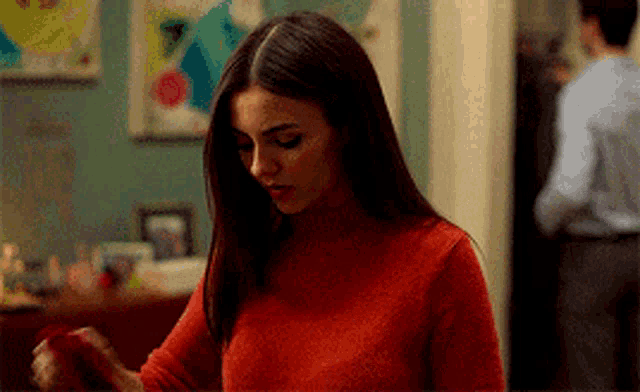 a woman in a red sweater is standing in a room looking down .