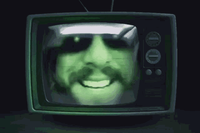 a man with a mustache and sunglasses is appearing on a television screen .