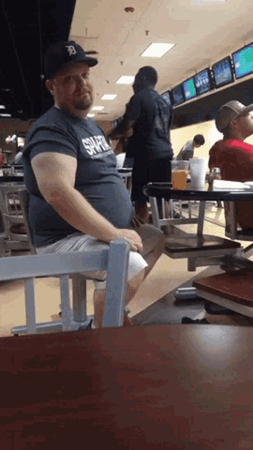 a man sits at a table in a bowling alley wearing a gray shirt that says tigers