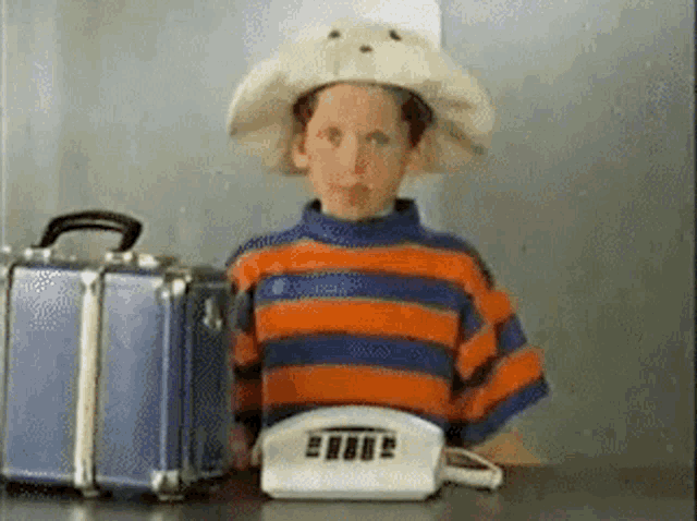 a young boy wearing a cowboy hat is holding a telephone and a suitcase