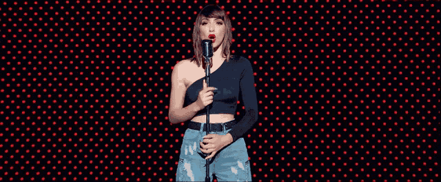 a woman singing into a microphone in front of a wall of red polka dots