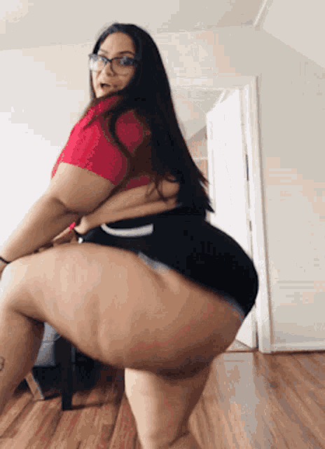 a woman in a red top and black shorts is dancing in a room