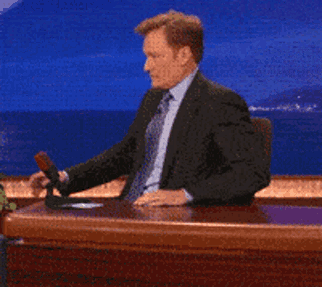 a man in a suit and tie is sitting at a desk with his arms outstretched