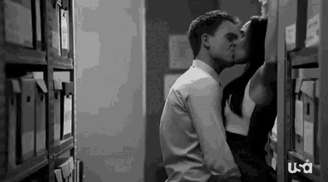 a man and a woman are kissing while sitting on a shelf .