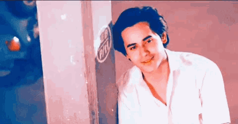 a man in a white shirt leaning against a wall with a sticker on it that says super pin