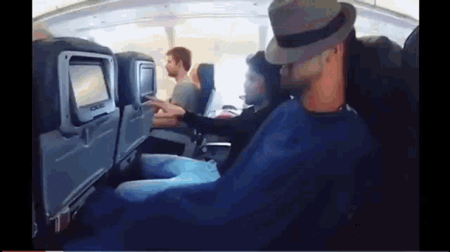 a man in a hat is holding another man 's hand on a plane
