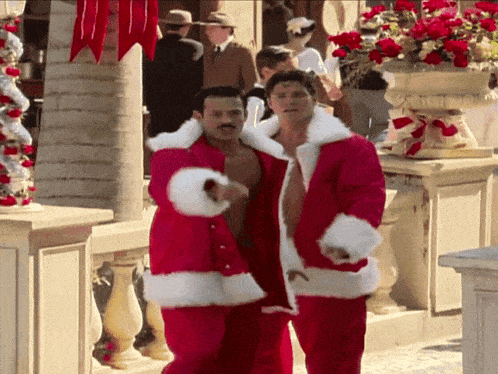 two shirtless men in santa suits are walking down a sidewalk
