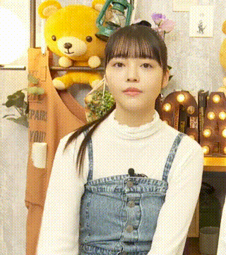 a young girl in a white shirt and denim overalls is standing in front of a teddy bear .