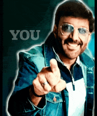 a man wearing sunglasses and a denim jacket pointing at the camera with the word you behind him
