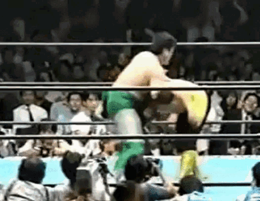 a man in a green shirt is wrestling another man in a yellow shirt in front of a crowd