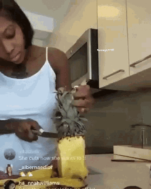 a woman is cutting a pineapple with a knife in a kitchen
