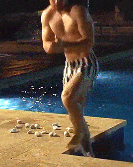 a shirtless man in striped shorts is standing on the edge of a swimming pool