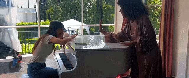 a woman is kneeling down next to a white piano while another woman stands behind it .
