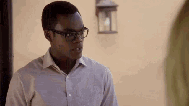 a young man wearing glasses and a white shirt is standing in front of a wall .