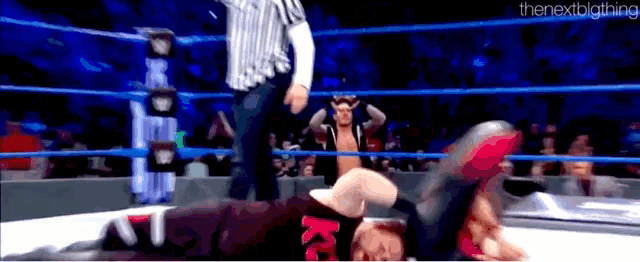 a man is laying on the ground in a wrestling ring while a referee watches .