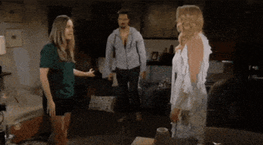 a man and two women are standing in a living room with a cbs logo on the wall