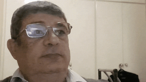 a man wearing glasses looks at the camera in a room