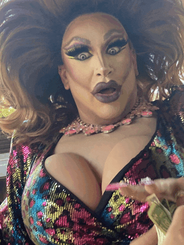 a drag queen in a sequined top is holding a dollar bill