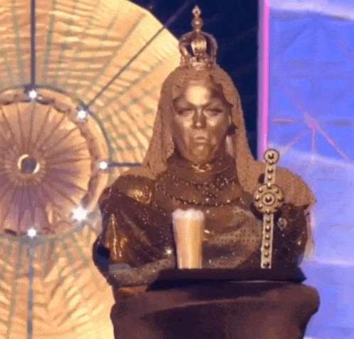 a gold statue of a woman with a crown on her head holding a candle