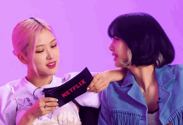 two women are sitting next to each other and one of them is holding a sign that says netflix .