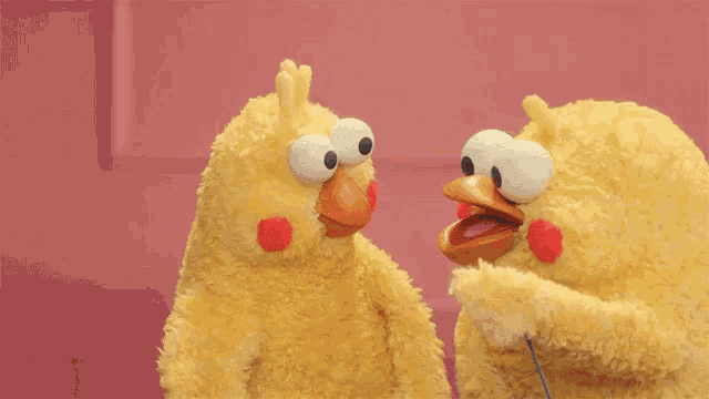 two stuffed birds are standing next to each other and looking at each other .