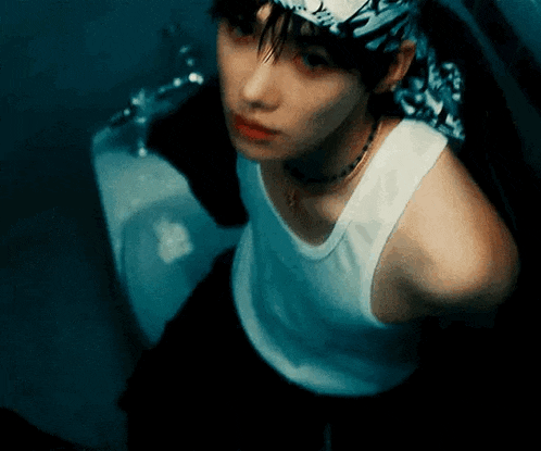 a young man wearing a white tank top and a bandana is sitting in a bathroom .