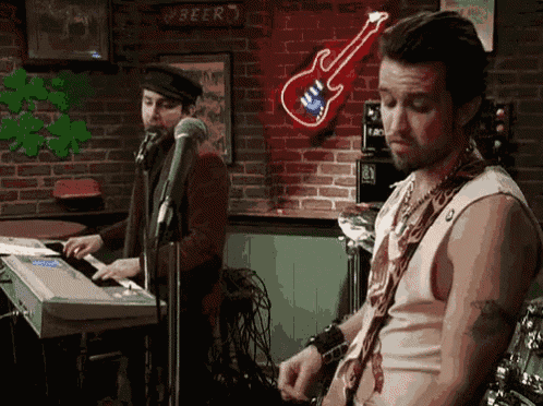 a man playing a keyboard and another man singing in front of a neon sign that says beer