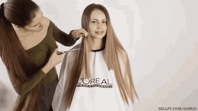 a woman is getting her hair cut by a hairdresser who is wearing a l' oreal cape .