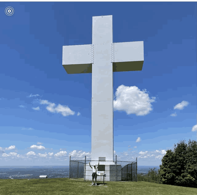 a man stands in front of a very large white cross