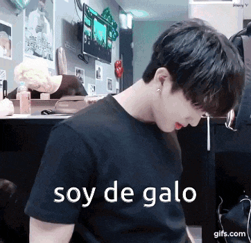 a young man in a black shirt is sitting at a desk with the words soy de galo written on the bottom .