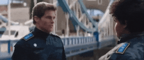 two police officers are standing next to each other in front of a bridge .