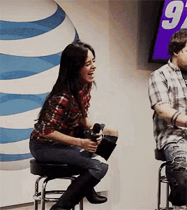 a woman sits on a bar stool laughing while a man sits in front of a screen with the number 9 on it