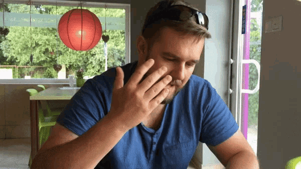 a man wearing sunglasses and a blue shirt is covering his face