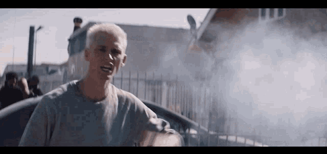a man is standing in front of a fence with smoke coming out of it and a building in the background .
